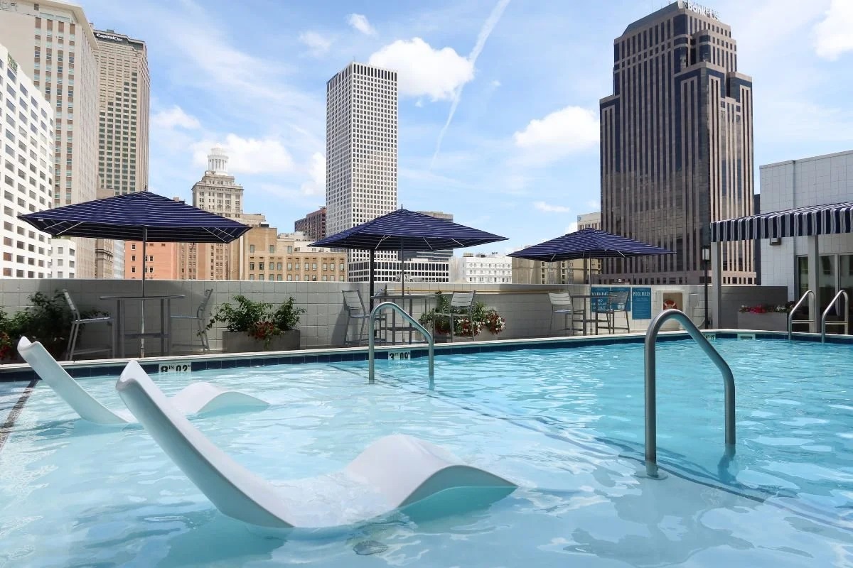 Rooftop pool with lounge chairs, umbrellas, and a city skyline in the background.