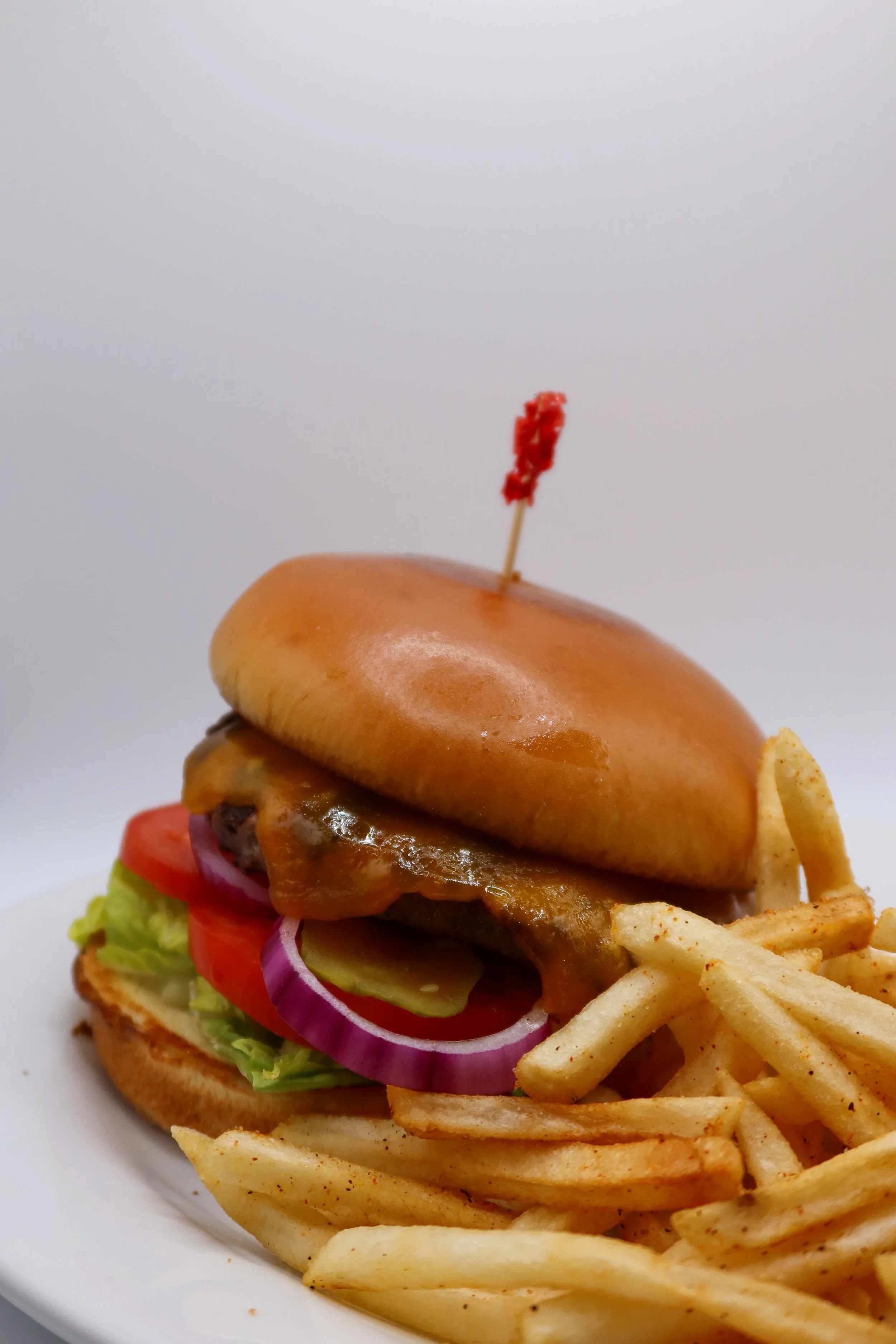 Cheeseburger with lettuce, tomato, onion, pickle, and fries on a white plate.