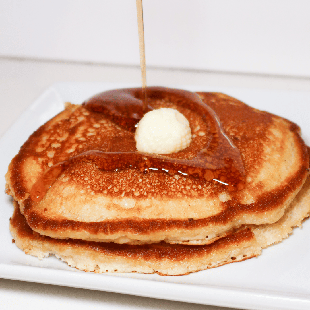 Stack of pancakes with butter and syrup on a white plate.