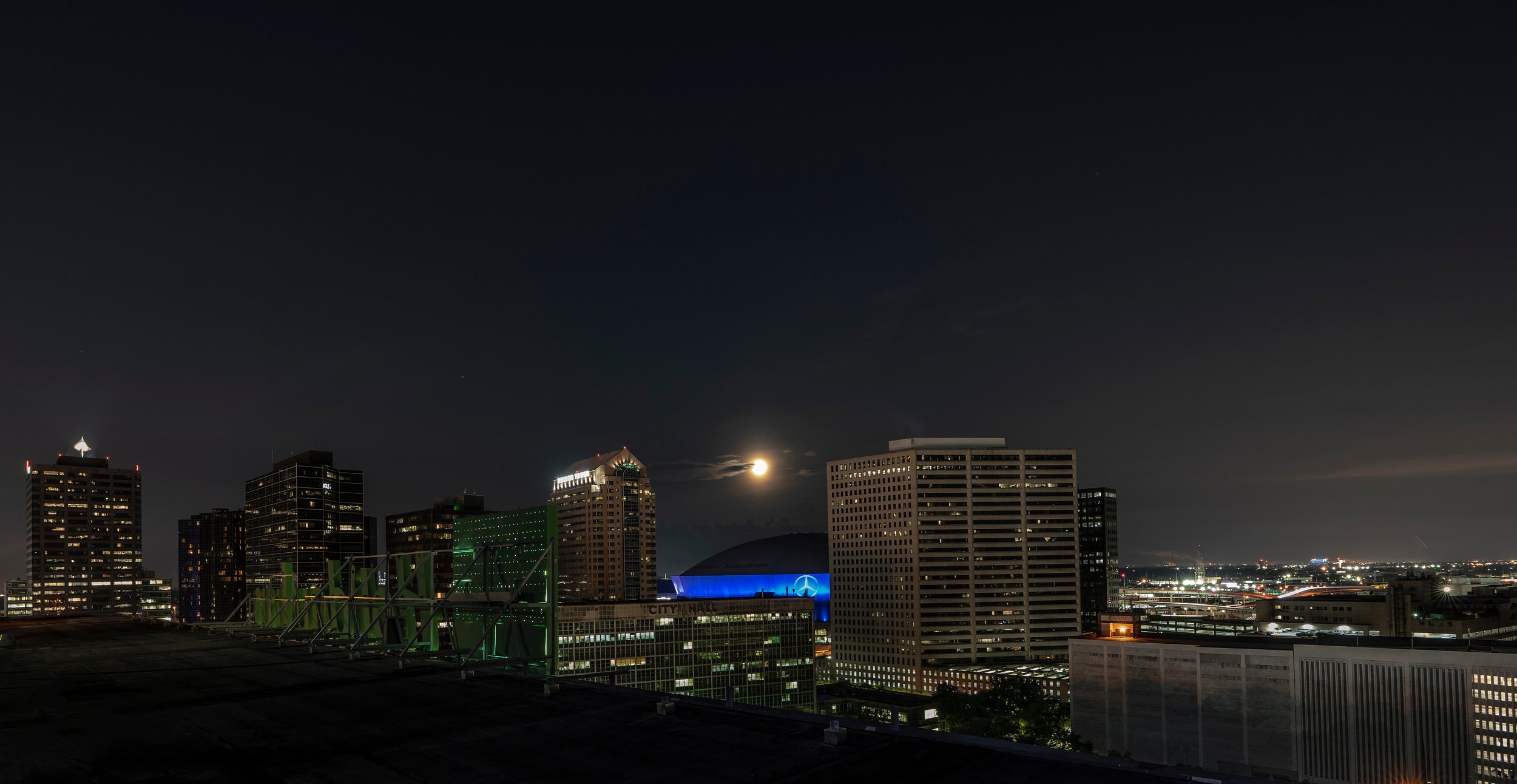 City skyline at night with a moonlit sky, illuminated skyscrapers, and a sports arena.