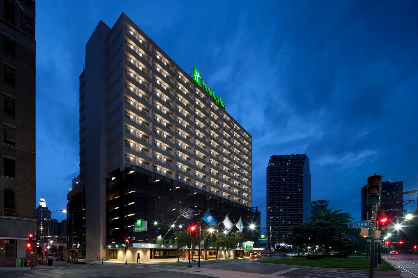 Night view of Holiday Inn hotel building with illuminated windows and neon sign, located at a street intersection, surrounded by other buildings and street lights.