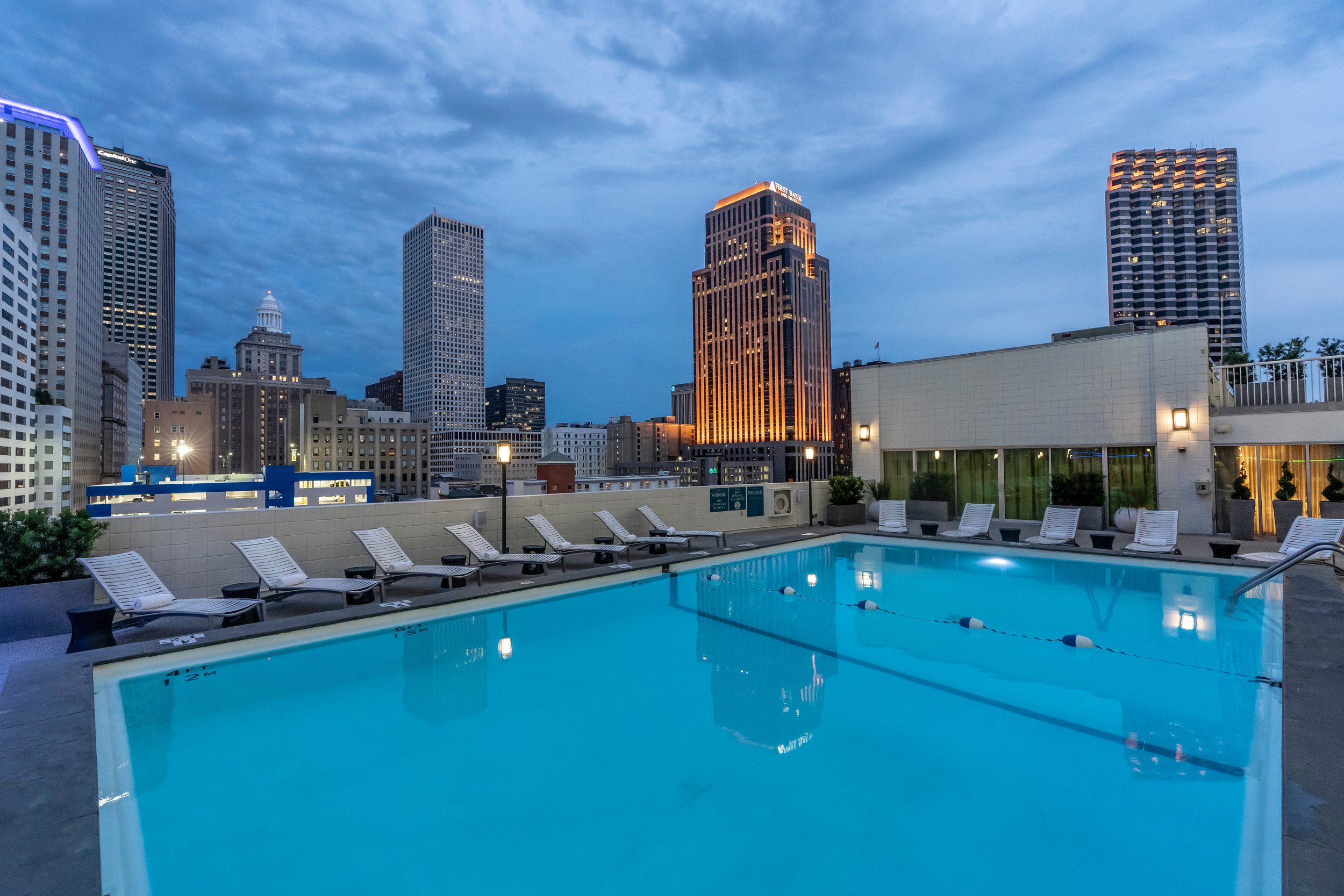 Rooftop pool with city skyline background featuring tall buildings lit up at dusk.